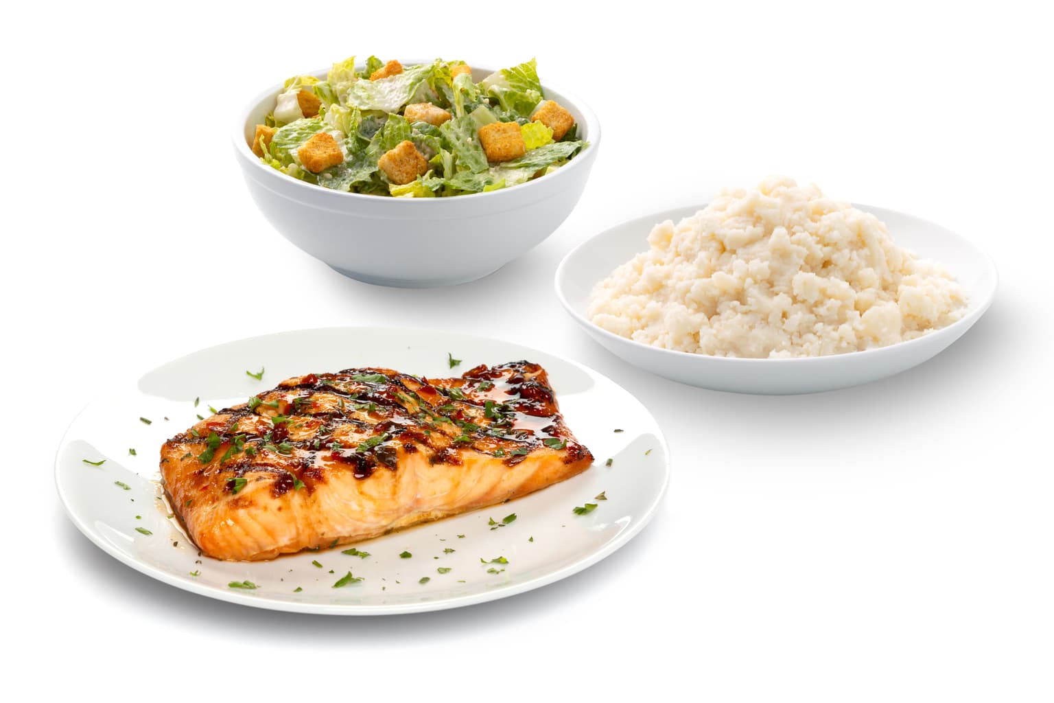 salmon filet on white plate with 2 sides caesar salad and mashed potatoes on white plates next to it.