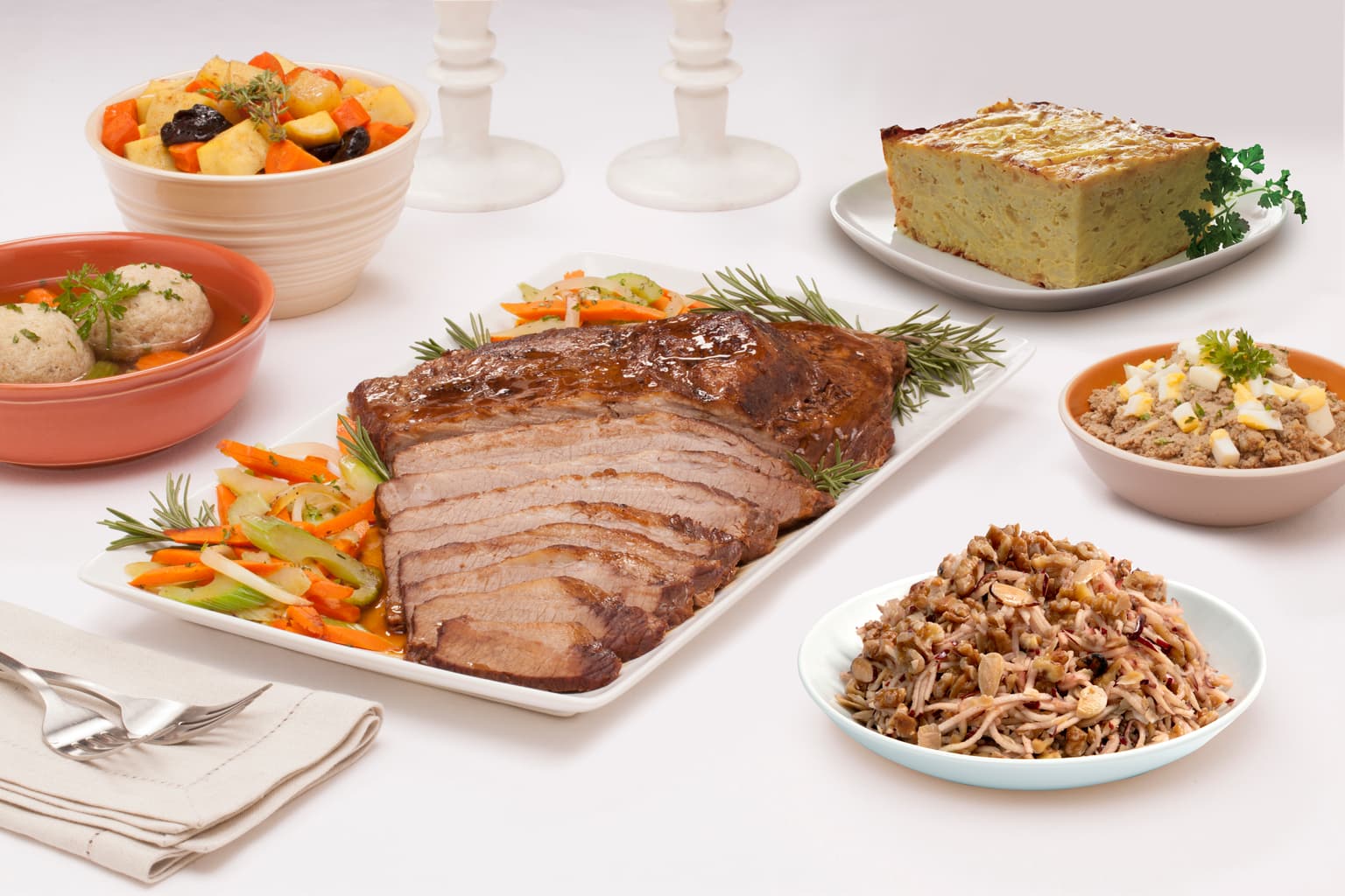 white plates with sliced brisket, latkes, matzo balls, tzimmes, charoses and chopped liver on a table
